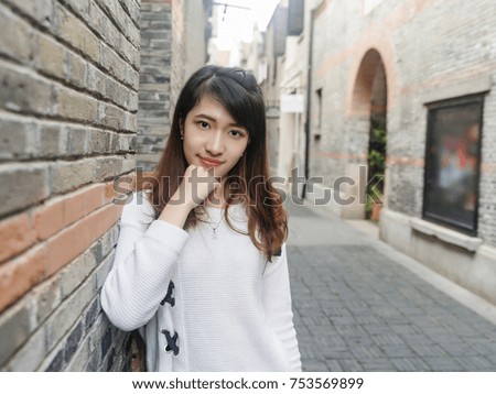 Portrait of beautiful young Chinese woman wearing white sweater and blue jeans in Shanghai Xintiandi, smiling with defocused Shikumen style street background,  Asian girl Concept ,Travel Concept.
