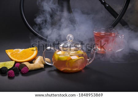 A closeup shot of a teapot with tea made with orange, berries and ginger