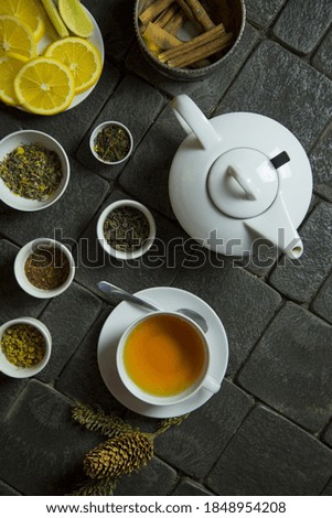 A vertical high angle shot of a cup of tea, a teapot, tea leaves, cinnamon and orange slices on the table
