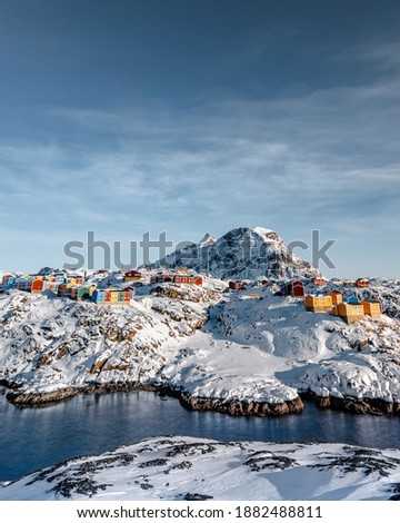A vertical shot of colorful houses on the snowy mountains near a frozen river in Greenland