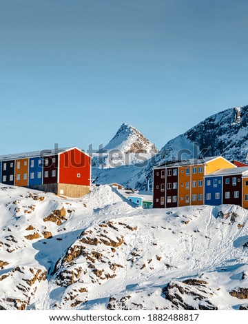 A vertical shot of colorful houses on the snowy mountains under the sunlight in Greenland