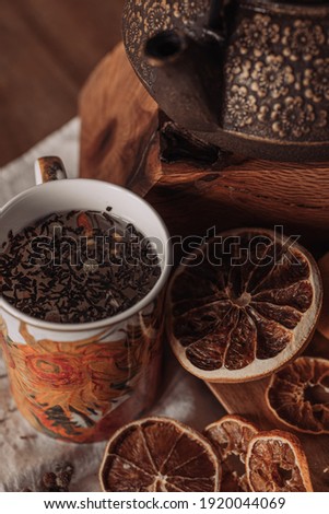 A vertical shot of a cup of tea with teapot and dry lemon slices