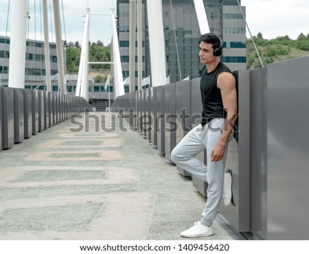 Sportsman listening to music while resting after jogging. Happy man feeling refreshed after exercise. Portrait of a multi ethnic man looking away in park after fitness.