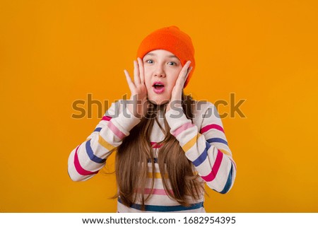Happy schoolgirl with long hair holds her hands in front on a yellow background