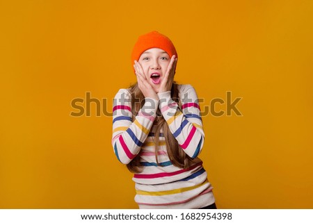 Happy schoolgirl with long hair holds her hands in front on a yellow background