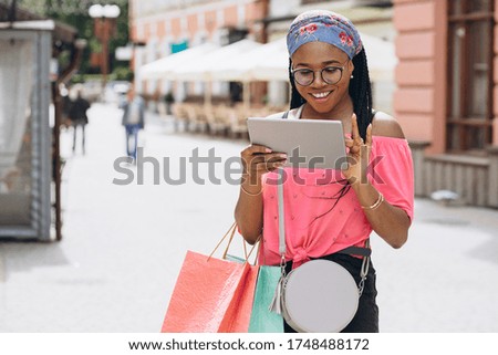 Happy young african american woman make shopping in the tablet and holding shopping bags on the street