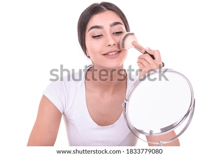 beautiful young smiling woman applying make up with makeup brush and looking her face in the mirror. isolated on white background.