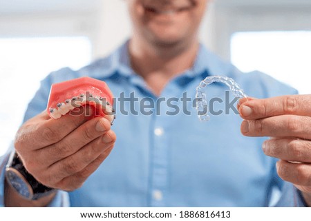 Dental care.Smiling orthodontist doctor holding aligners and braces in hand shows the difference between them