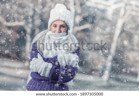 Portrait of happy woman in warm clothing on snowing winter day outdoors. Snowflakes falling on cheerful girl wearing wool cap, scarf and sweater.Female person in cold weather.