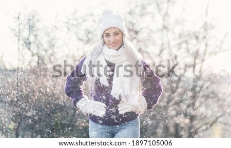 Beautiful young woman wearing warm clothing in snowflakes and winter day outdoors. Half length of cute girl wearing wool cap, scarf and purple sweater. Female person in cold weather.