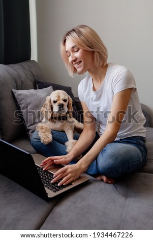 belle jeune femme en T-shirt blanc à la maison sur un canapé gris avec un ordinateur portable et un chien