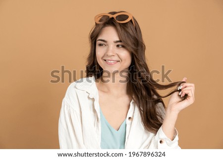 Beautiful girl with glasses on her head, she looks away, playing with her hair. Cute lady on a brown background