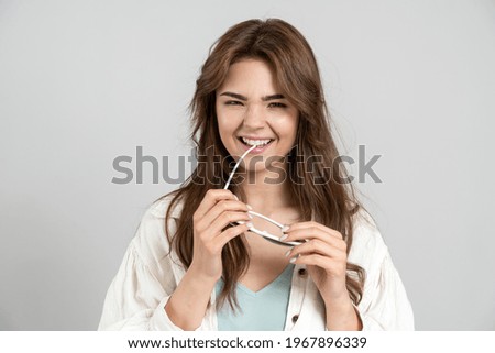 Playful, cute lady holding sunglasses in her hands. Beautiful girl posing on a gray background