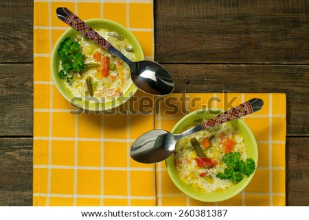 Two bowls of vegetable soup with cheese on a yellow napkin and a wooden table