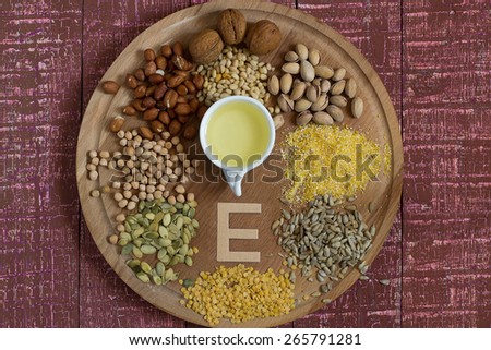 Food sources of vitamin E (corn, peanuts, pistachios, walnuts and pine nuts, sunflower and pumpkin seeds, lentils, peas, oil) on a round board and white background