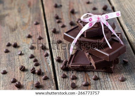 Pyramid of chocolate pieces, tied with a ribbon, chocolate drops on a wooden surface. Selective focus