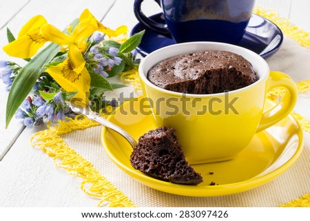 Quick cupcake in a yellow cup, cooked in a microwave oven, a blue cup with tea and flowers on white wooden background. Selective focus