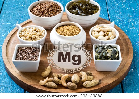 Collection products containing magnesium (buckwheat, cashews, peanuts, pine nuts, almonds, flax seeds and pumpkin, mustard, seaweed) on a round cutting board and a blue wooden background