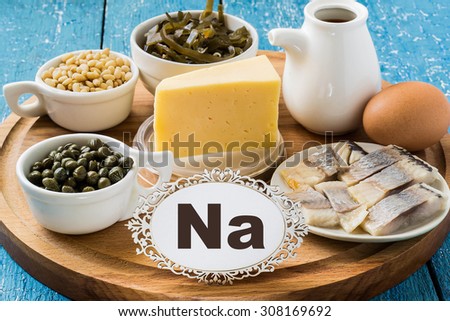 Products containing sodium (seaweed, salted herring, capers, pine nuts, soy sauce, egg) on a round cutting board and a blue wooden background