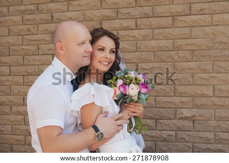 Sensual portrait of a beautiful bride and groom with a beautiful wedding bouquet on a background of a brick wall