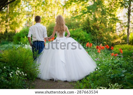 The bride and groom are in the park holding hands around the beautiful flower beds of poppies and white flowers