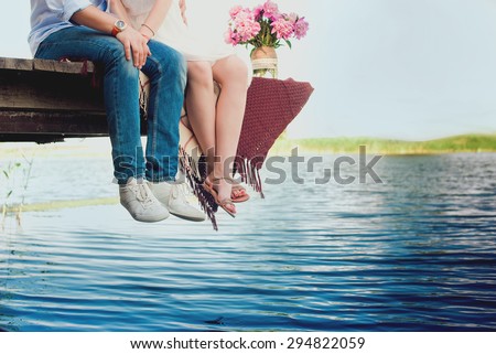 Pretty strong young loving couple sitting on the bridge over the river, next to a bouquet of peonies, lifestyle, concept, love, tenderness