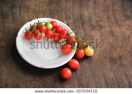 Multicolored cherry tomatoes in white plate on a wooden background, of vegetarian food, vegetables