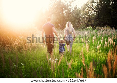 Young healthy parents mom and dad holding his son\'s hand, embrace and walk together outdoors in sunset light, family, lifestyle, happiness, love, the future