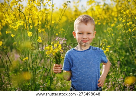 Little happy boy with a bouquet of flowers is in the yellow flowering rapeseed field