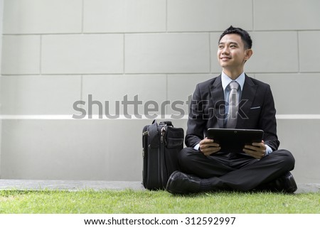 Asian business male using portable computer on park of city. He is looking