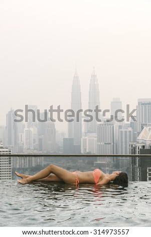 Beautiful woman in swimming pool watching the city. Kuala Lumpur with Twin Towers