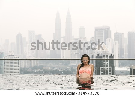 Beautiful woman in swimming pool watching the city. Kuala Lumpur with Twin Towers