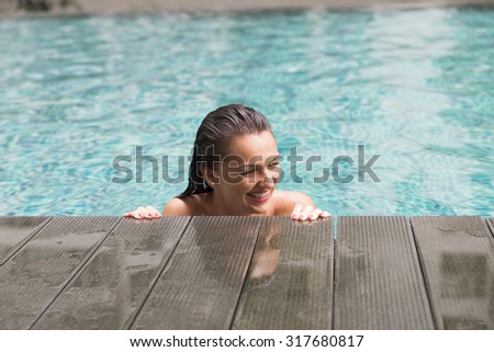 Beautiful young woman smiling in a swimming pool, under the golden summer light.