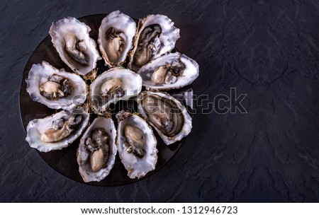 Open oysters on black round plate on dark grey background. Fresh Oysters close-up top view. Healthy sea food. Oyster dinner with champagne in restaurant. Luxury food. Foto stock © 