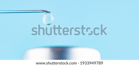 Vaccine drop on syringe needle. Vaccination concept, disease prevention. Needle with a drop of vaccine on a blue background