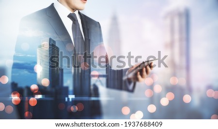 Freelance mobile working concept with man in black suit looking at digital tablet on blurry megapolis city background. Double exposure
