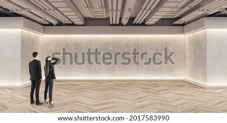 Businessmen and women looking at wall in modern exhibition space concrete interior with mockup place and wooden flooring. Mock up