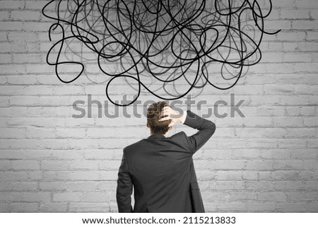 Back view of businessman looking at abstract scribble on brick wall background. Question, think and confusion concept