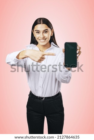 Mobile application concept with smiling businesswoman in white shirt showing modern cellphone with blank screen on abstract pink background, mockup