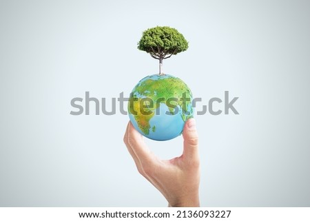 Close up of female hand holding abstract globe with tree on light background. World, earth, ecology and planet concept