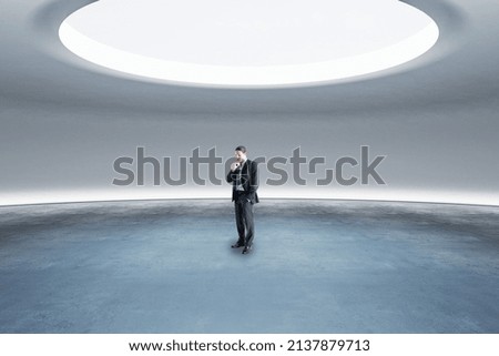Thoughtful young european businessman standing in abstract space ship interior with spotlight from above. Presentation concept