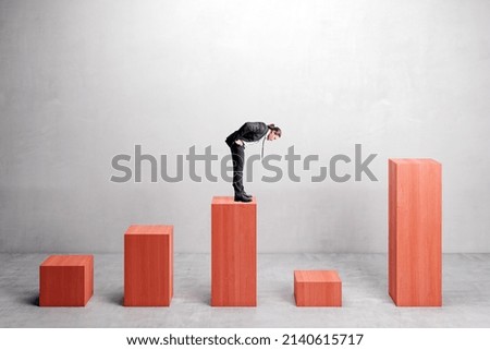 Businessman on red chart bars on concrete wall background. Crisis, business and growth concept