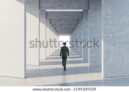 Way to success and victory concept with walking businessman back view in modern architecture designed tunnel with bright light spot in the end