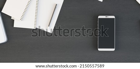 Le téléphone portable à écran vierge est sur la table de bureau en bois foncé avec des fournitures, vue au-dessus. Montage, rendu 3D