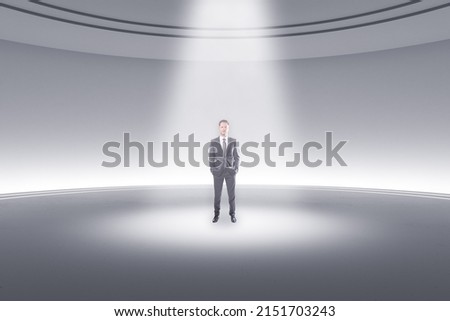 Thoughtful young businessman standing in abstract light round pedestal interior with spotlight