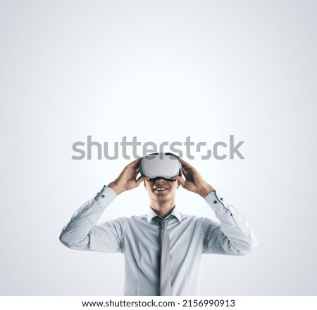 Virtual reality concept with young businessman gets new emotions in VR glasses on abstract light grey background and empty space on his head for you text, mock up