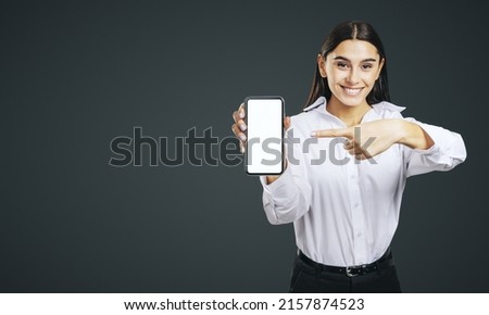 Mobile application concept with smiling businesswoman in white shirt showing modern smartphone with white blank screen on abstract dark background with place for your logo or text, mock up