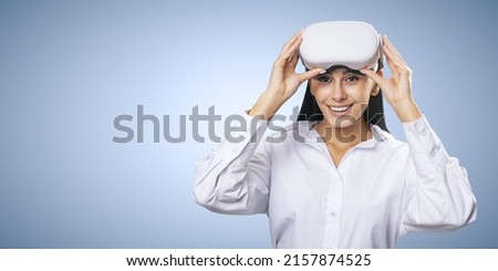 Virtual reality concept: smiled young woman in light shirt with VR glasses on her head on light blue background with place for your logo or text, mockup
