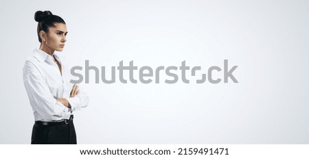 Resentment and unpleasant emotions concept with stressed young woman in white shirt crossing her arms isolated on light grey background with blank place for you logo or text, template