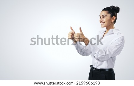 Like concept with happy girl in white shirt holding thumbs up on light grey background with empty place for you text, mock up